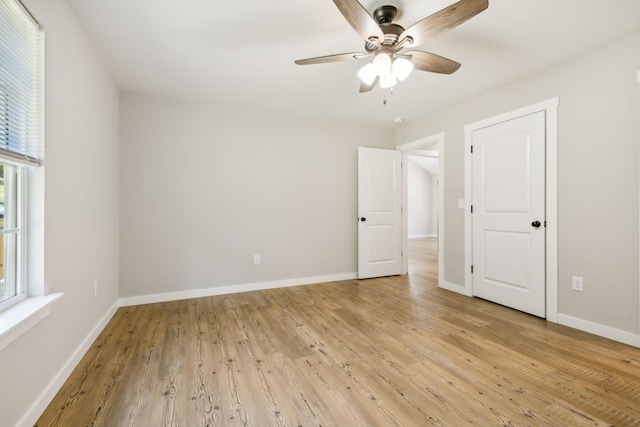 spare room with light wood finished floors, a ceiling fan, and baseboards