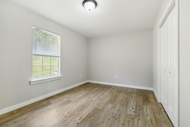 unfurnished bedroom with a closet, visible vents, wood finished floors, and baseboards
