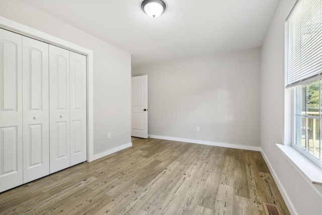 unfurnished bedroom with a closet, visible vents, wood finished floors, and baseboards