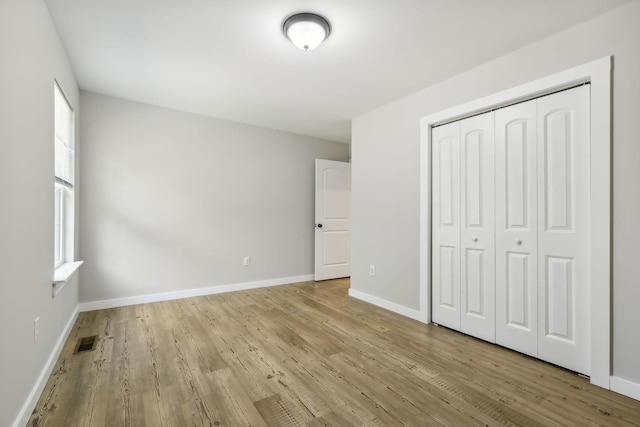 unfurnished bedroom featuring a closet, visible vents, wood finished floors, and baseboards
