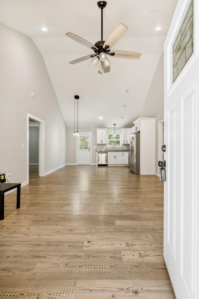 unfurnished living room with baseboards, high vaulted ceiling, a ceiling fan, and light wood-style floors