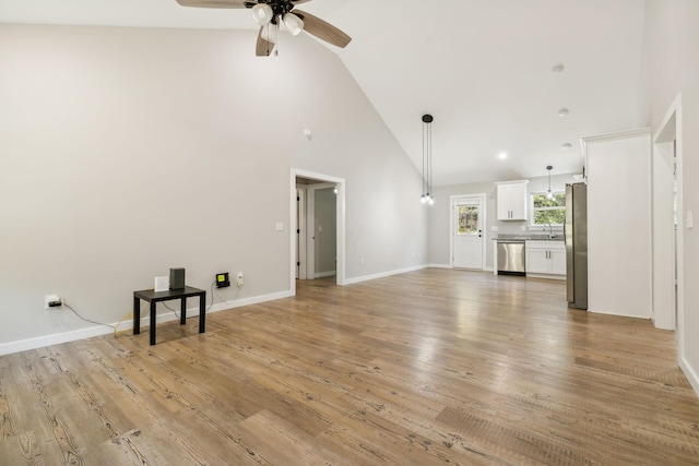 unfurnished living room with a sink, high vaulted ceiling, a ceiling fan, light wood-style flooring, and baseboards