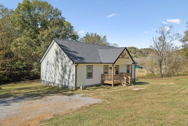 rear view of house featuring a lawn, a deck, and a shingled roof