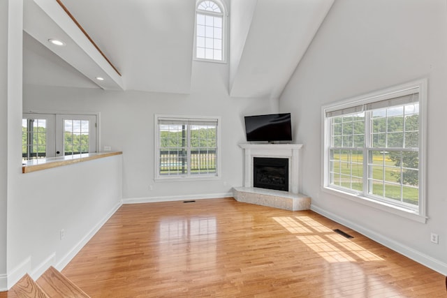 unfurnished living room featuring wood finished floors, a glass covered fireplace, baseboards, visible vents, and high vaulted ceiling