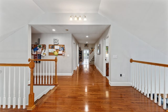 hallway featuring baseboards, stairway, wood finished floors, and lofted ceiling