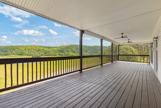 wooden terrace featuring ceiling fan, a view of trees, and a lawn