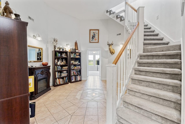 stairs with visible vents, baseboards, a glass covered fireplace, tile patterned flooring, and a high ceiling