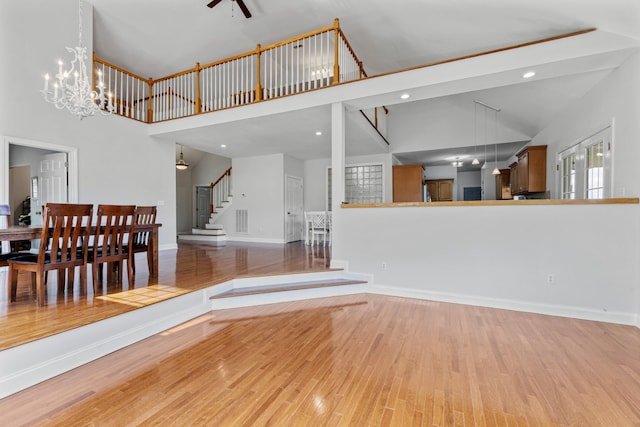 unfurnished living room featuring wood finished floors, stairs, ceiling fan, baseboards, and high vaulted ceiling