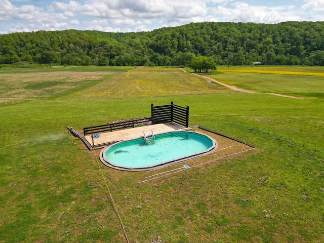 view of pool featuring a rural view, a yard, and a wooded view