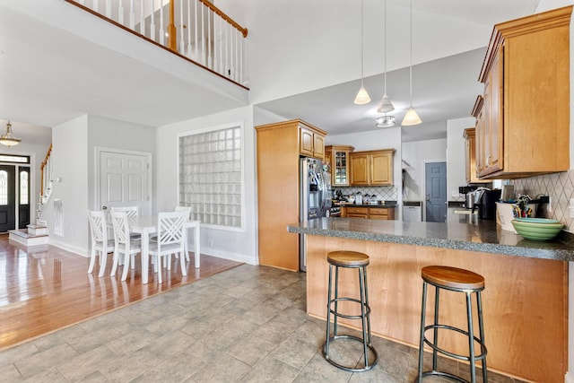 kitchen with tasteful backsplash, stainless steel fridge, dark countertops, a kitchen bar, and a peninsula