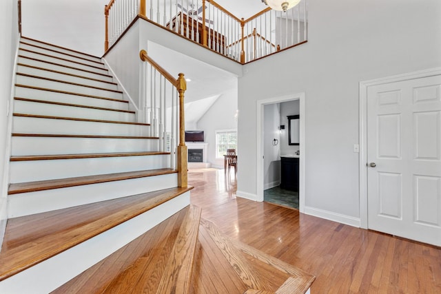 staircase with a fireplace, a towering ceiling, wood finished floors, and baseboards