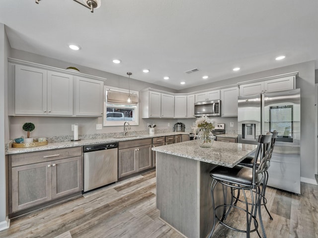 kitchen with a kitchen breakfast bar, a sink, appliances with stainless steel finishes, visible vents, and light wood-type flooring