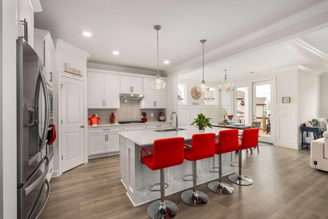4372 Spregan Way, Smyrna, TN 37167 - kitchen with under cabinet range hood, appliances with stainless steel finishes, a kitchen bar, a sink, and light wood-type flooring