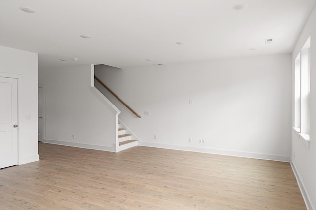 unfurnished living room featuring stairway, light wood-style floors, and plenty of natural light