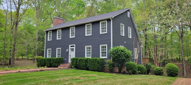 colonial house featuring a chimney, a front yard, and a wooded view