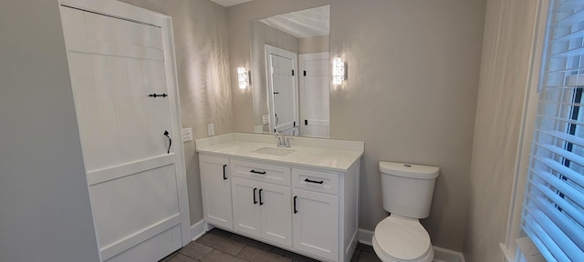 half bath with toilet, tile patterned flooring, vanity, and baseboards
