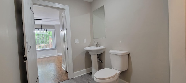 half bath featuring wood finished floors, toilet, and baseboards