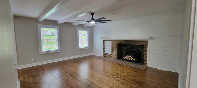 unfurnished living room with wood finished floors, beamed ceiling, ceiling fan, a brick fireplace, and baseboards