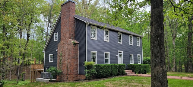 view of property exterior featuring a lawn, a chimney, central air condition unit, and a wooden deck