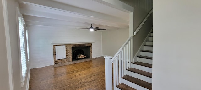 unfurnished living room with beamed ceiling, a healthy amount of sunlight, a ceiling fan, stairs, and wood finished floors