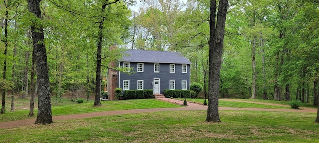 colonial-style house featuring a chimney and a front lawn