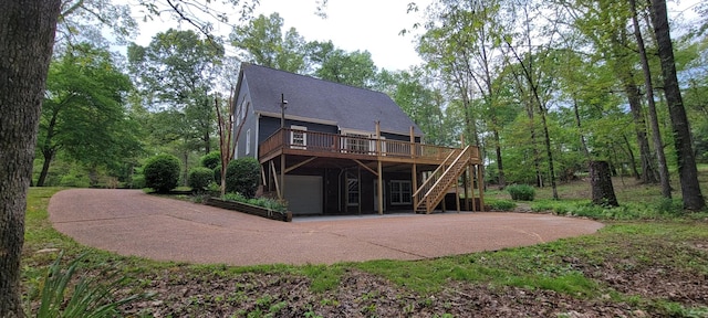 rear view of house with an attached garage, concrete driveway, stairs, and a wooden deck