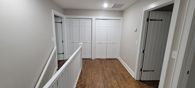 corridor with baseboards, visible vents, an upstairs landing, and dark wood-style flooring