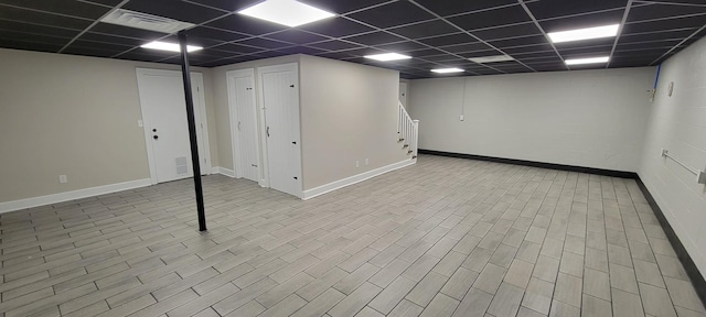 finished below grade area with stairway, visible vents, baseboards, wood finished floors, and a paneled ceiling