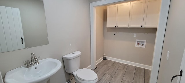 half bathroom featuring toilet, a sink, wood finished floors, and baseboards