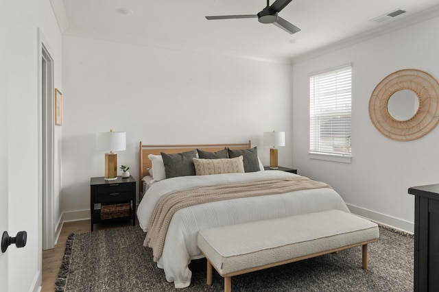 bedroom with wood finished floors, ornamental molding, ceiling fan, baseboards, and visible vents