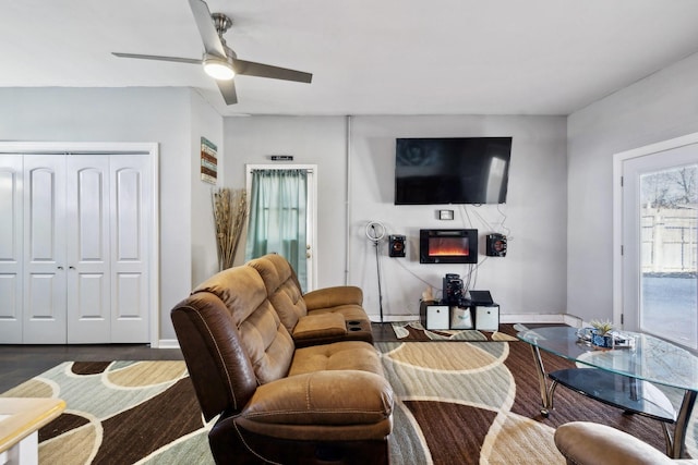 living room with a glass covered fireplace, wood finished floors, ceiling fan, and baseboards