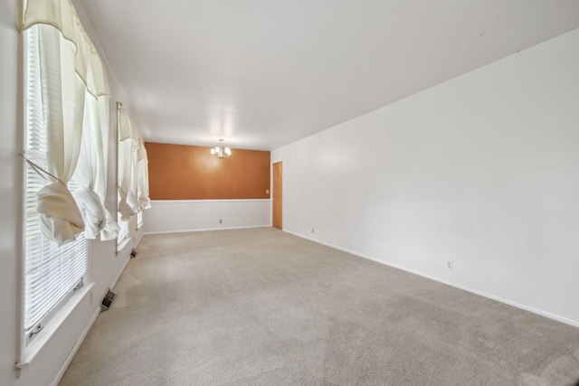 spare room with light carpet, baseboards, and a chandelier