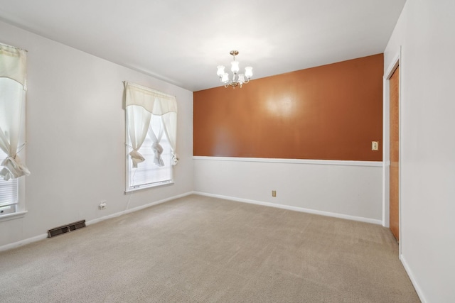 spare room featuring a chandelier, carpet floors, and baseboards
