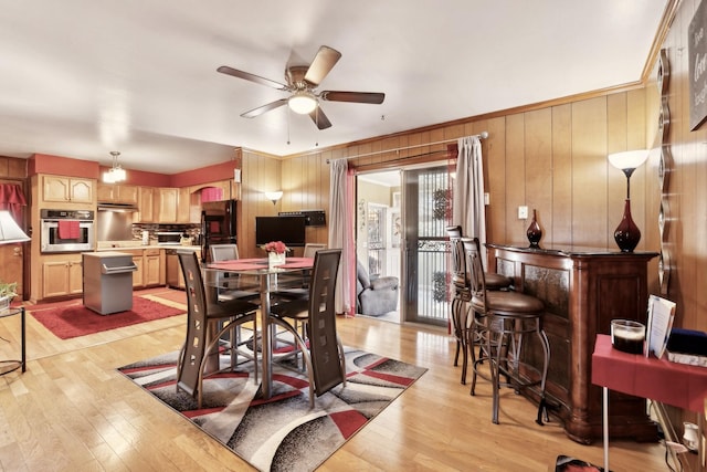 dining space with a ceiling fan, light wood-style floors, wooden walls, and a dry bar