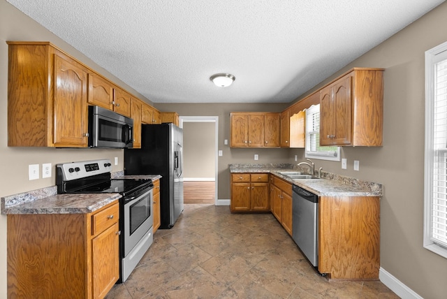 2938 Heatherfield Dr, Woodlawn, TN 37191 - kitchen featuring appliances with stainless steel finishes, a sink, baseboards, brown cabinets, and a textured ceiling