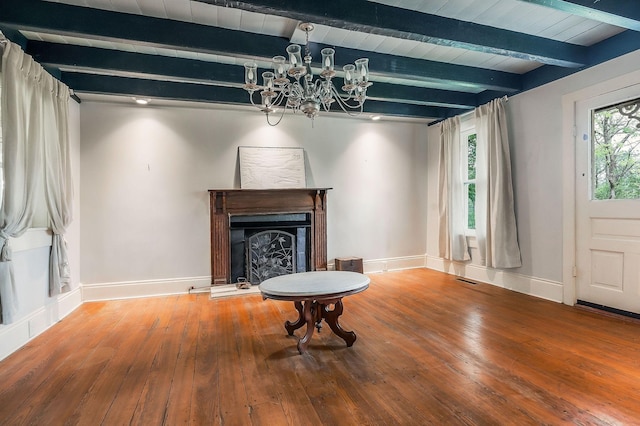 living area with beam ceiling, a chandelier, a fireplace with raised hearth, baseboards, and hardwood / wood-style flooring