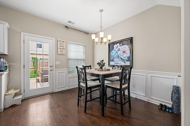 dining space with a decorative wall, wainscoting, visible vents, a notable chandelier, and dark wood-type flooring
