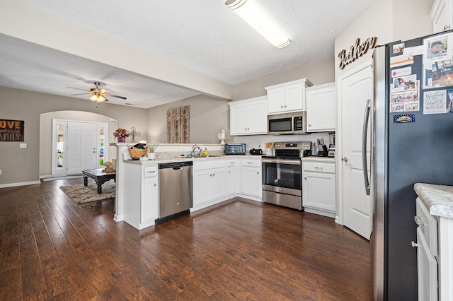 kitchen with a peninsula, stainless steel appliances, white cabinetry, a textured ceiling, and dark wood-style floors