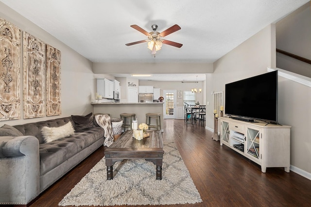 living room featuring dark wood-type flooring, baseboards, and ceiling fan with notable chandelier