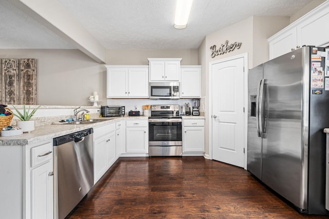 kitchen featuring white cabinets, a sink, stainless steel appliances, dark wood finished floors, and a peninsula