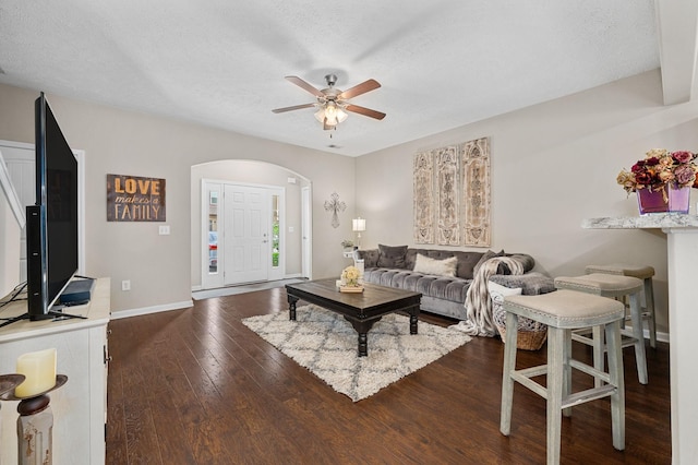 living room featuring dark wood-style flooring, ceiling fan, a textured ceiling, baseboards, and arched walkways