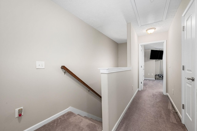 hallway featuring attic access, an upstairs landing, carpet, baseboards, and a textured ceiling