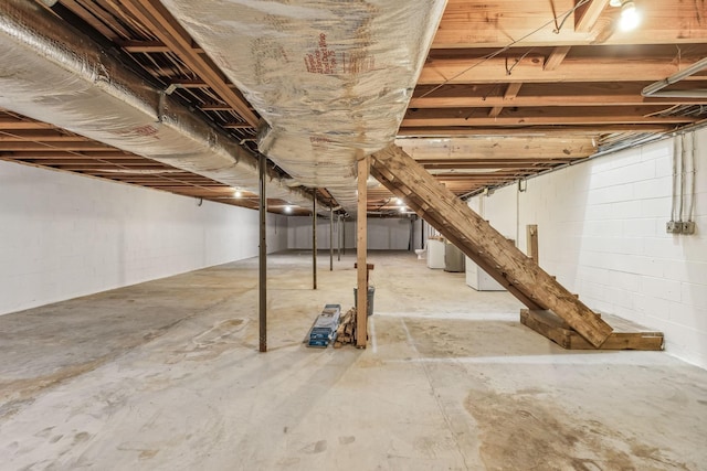 unfinished below grade area featuring stairway, concrete block wall, and water heater