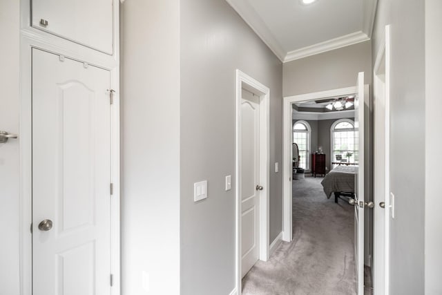 hall featuring baseboards, ornamental molding, and light colored carpet