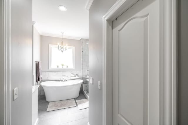 bathroom with tile walls, tile patterned floors, a chandelier, ornamental molding, and a soaking tub