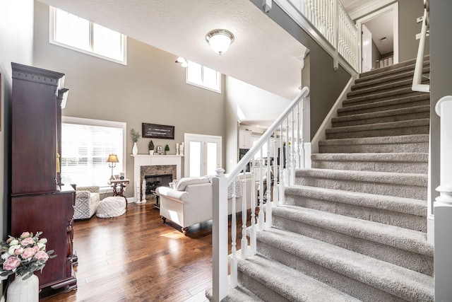 stairs featuring a high end fireplace, baseboards, hardwood / wood-style floors, and a towering ceiling