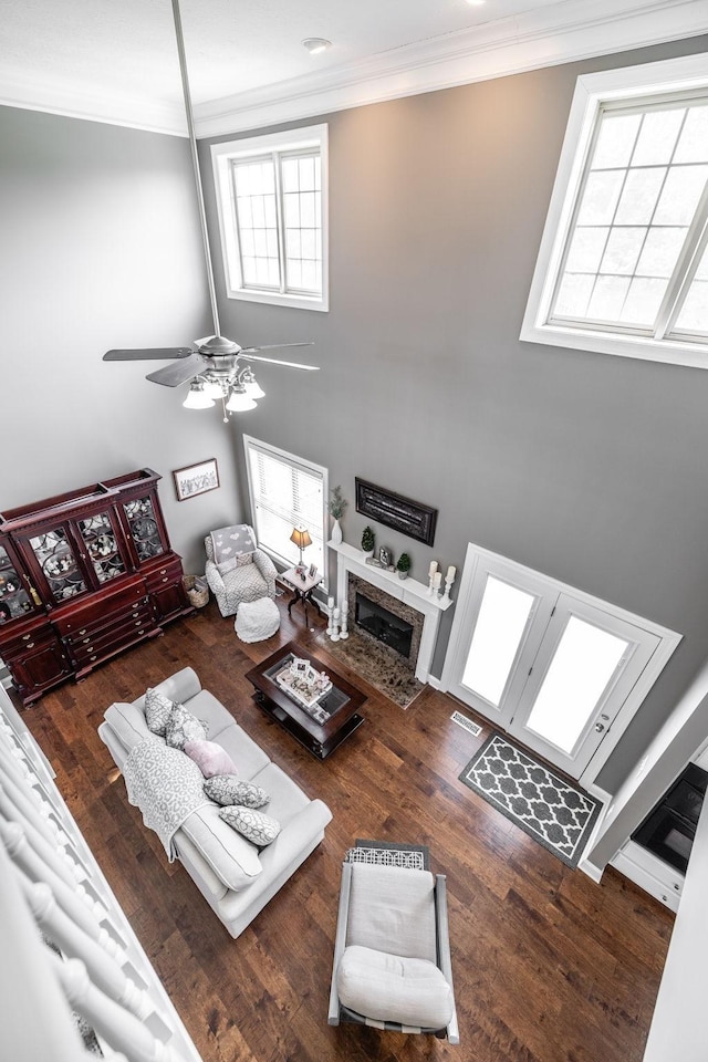 living room featuring ornamental molding, a fireplace, a ceiling fan, and a towering ceiling