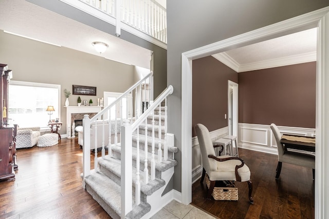 staircase with ornamental molding, wood finished floors, a fireplace, and a wainscoted wall