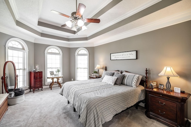 carpeted bedroom with a raised ceiling, ornamental molding, and a ceiling fan