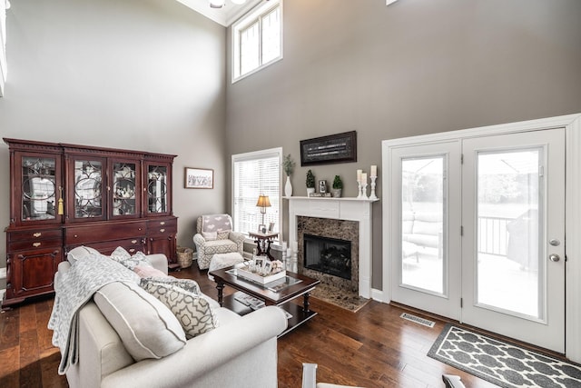 living area featuring a towering ceiling, a fireplace, dark wood-style flooring, and visible vents